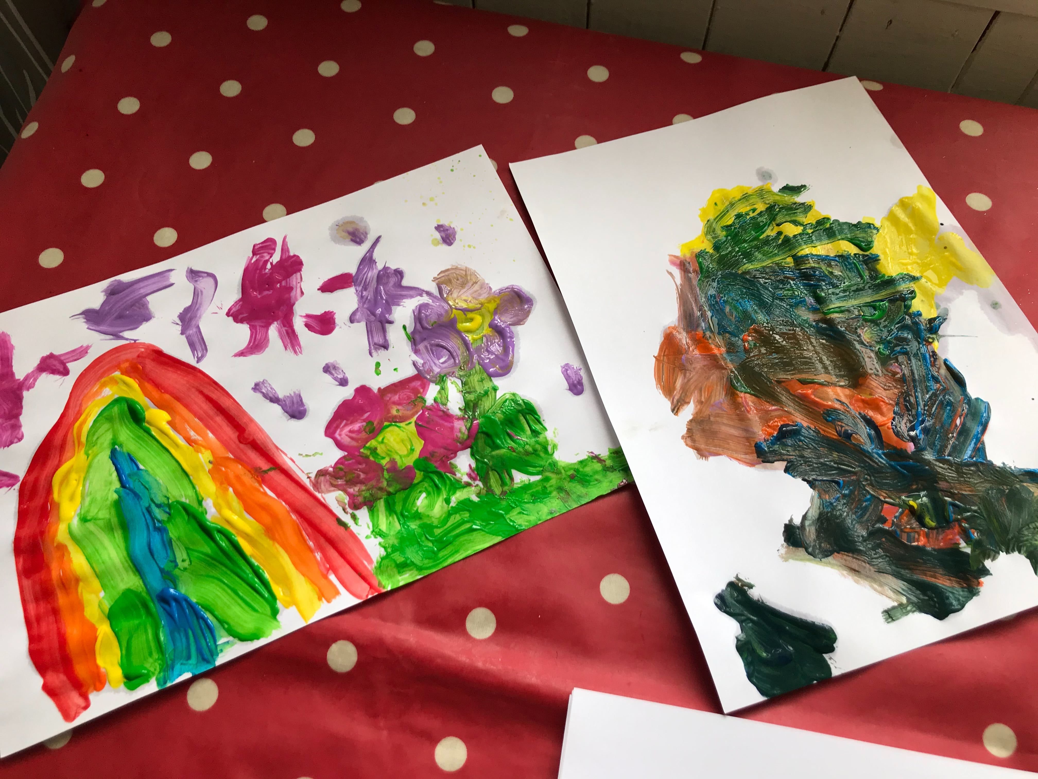 Two children's paintings of colourful rainbows on a table
