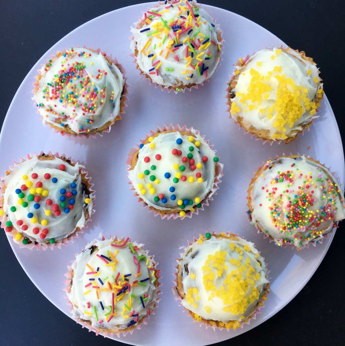 8 vanilla cupcakes with white icing and rainbow sprinkles, sitting on a white plate